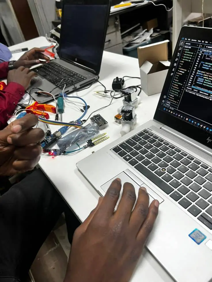 Hands wiring sensors to a circuit board beside a laptop running code